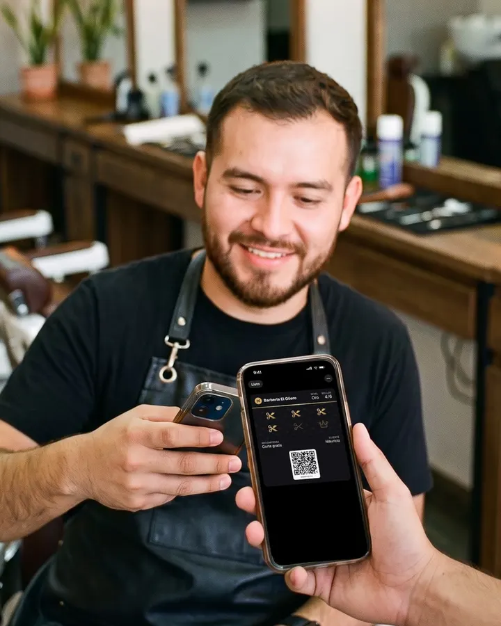 Un barbero escanea con su celular la tarjeta de sellos que su cliente le muestra en el iPhone.